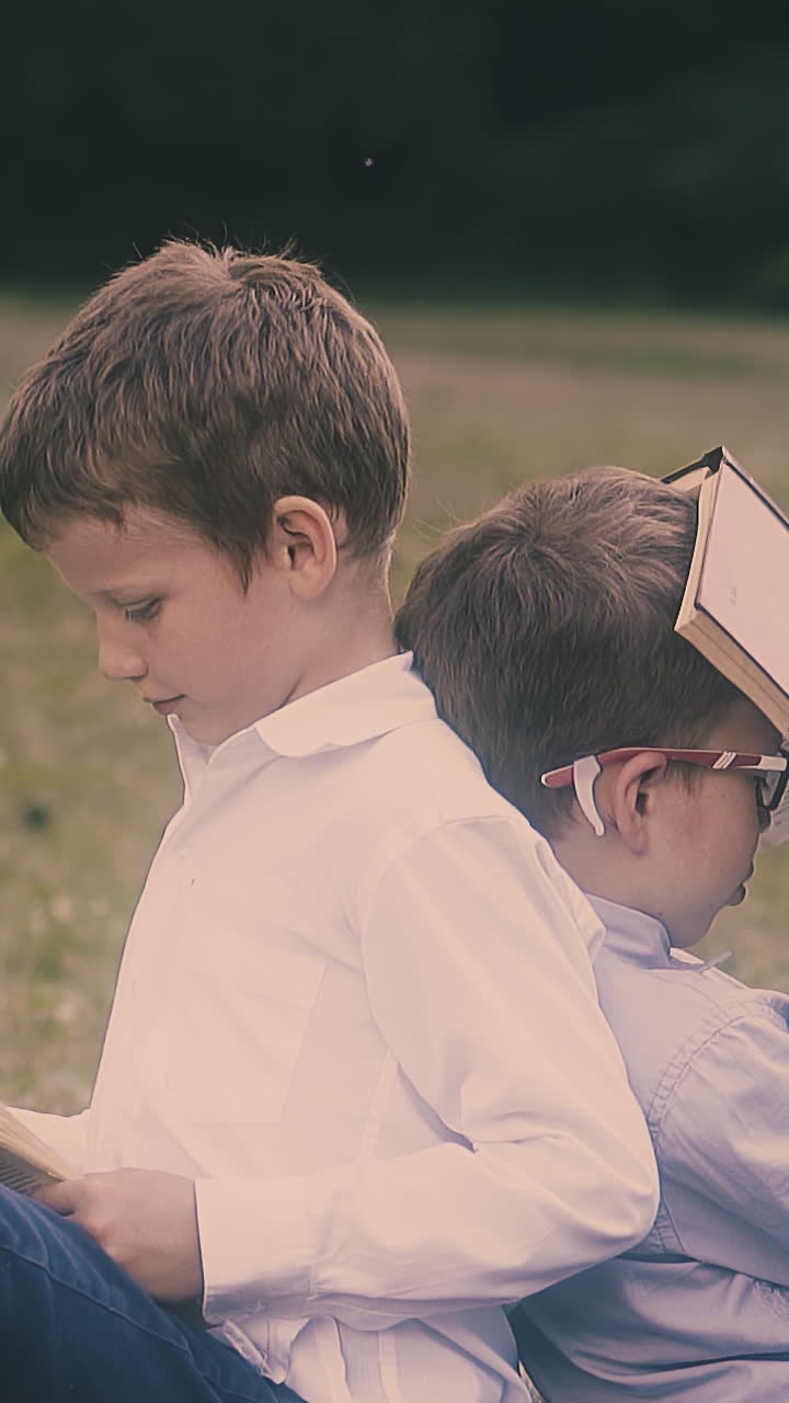 nice junior schoolboys in uniform prepare for hard exam sitting on green grass on warm day close view slow motion