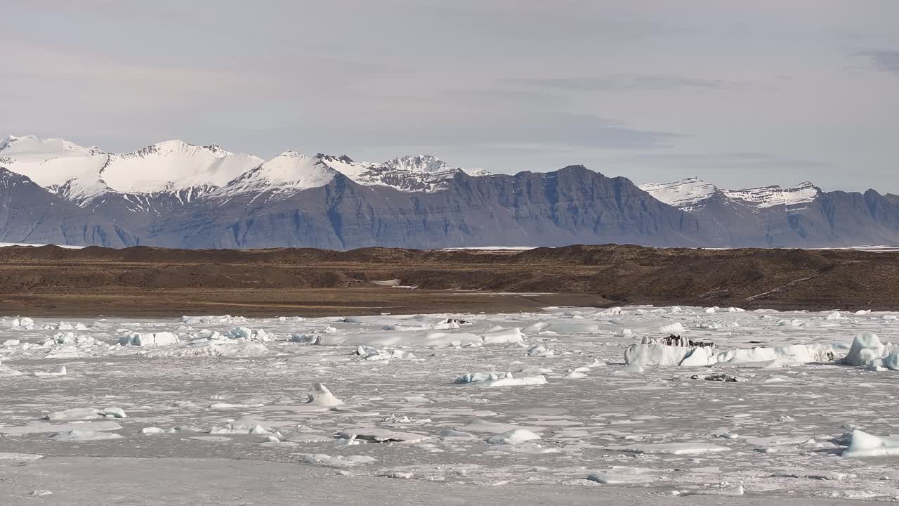 Lateral drone movement revealing the icy expanse of Fjallsárlón glacier lagoon with snow-covered mountains in the background, Vatnajökull, Iceland.