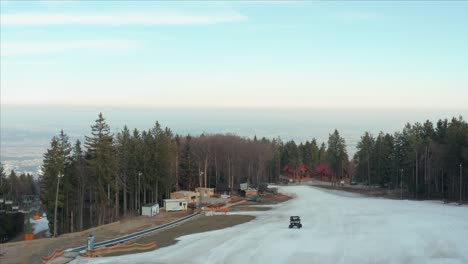 Empty-Ski-Lift-With-Small-Vehicle-Traveling-On-Winter-Road-By-Shaggy-Forest-At-Countryside