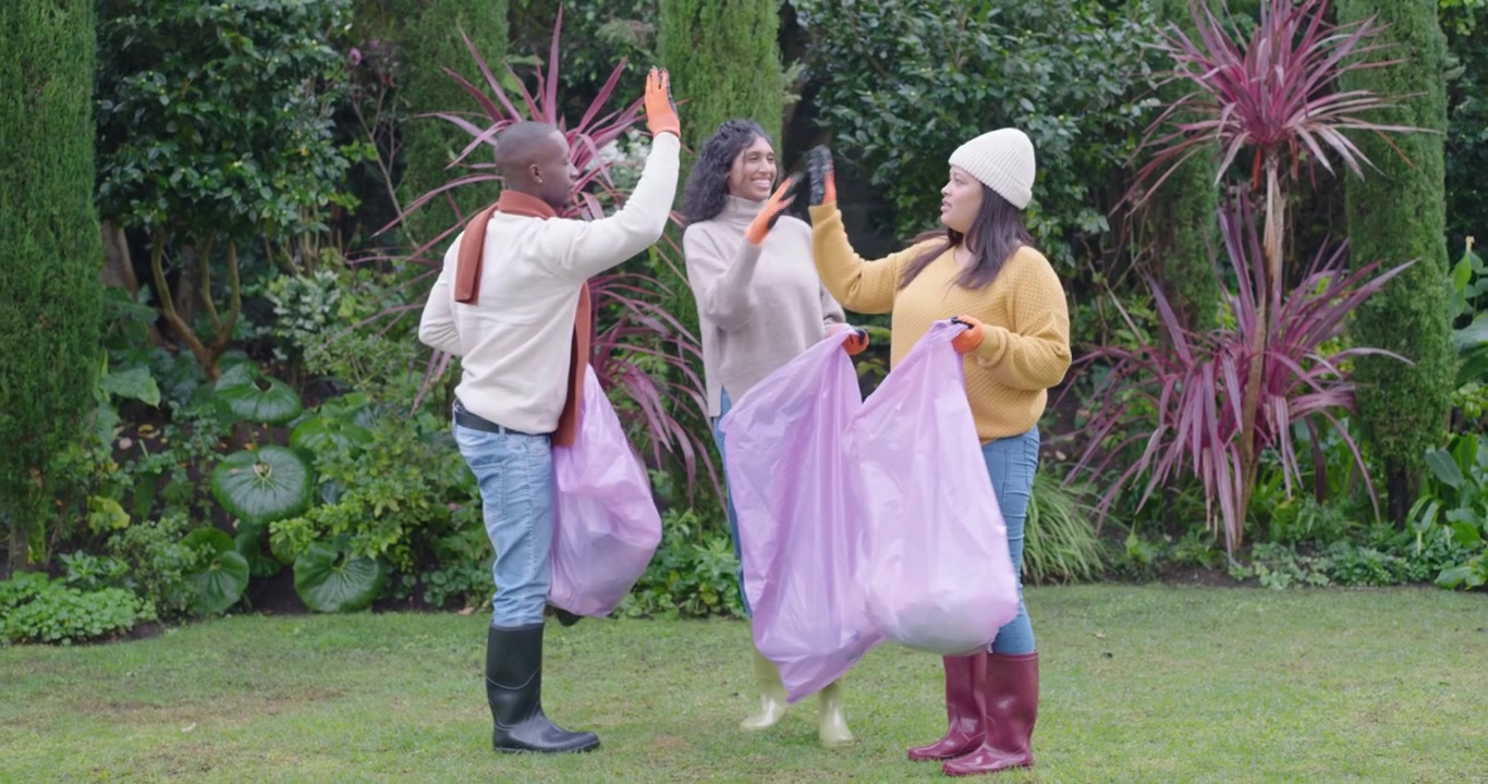 Diverse volunteers walking on lawn with purple sacks, spotting litter, picking it up to clean