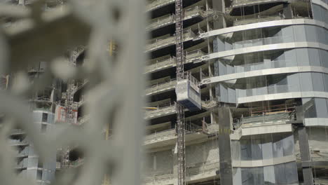 An-observation-of-a-skyscraper-under-construction-in-Dubai,-UAE,-depicts-a-crane-hoisting-workers-atop-the-towering-structure,-which-typically-reaches-a-height-of-180-meters-upon-completion