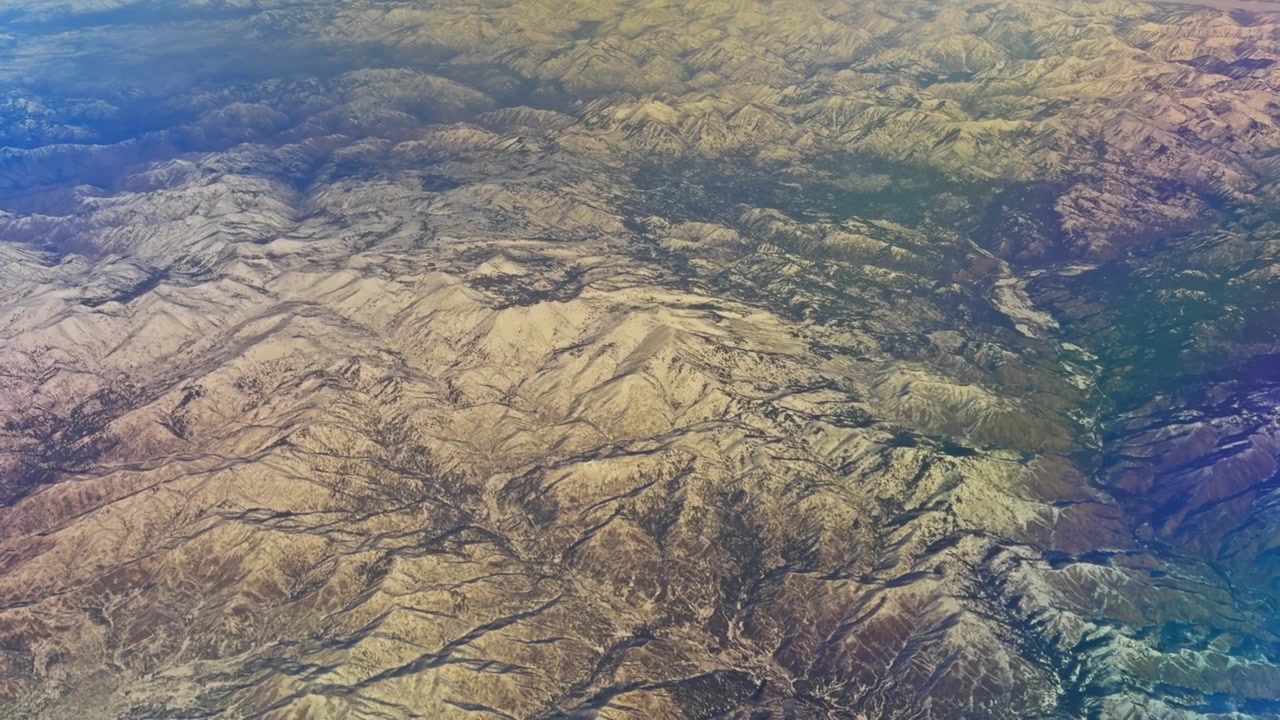 Cumes de montanhas e vales iluminados pelo sol estendendo-se por um terreno acidentado abaixo, vista aérea.