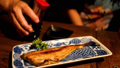 hand pouring sauce over grilled fish dish