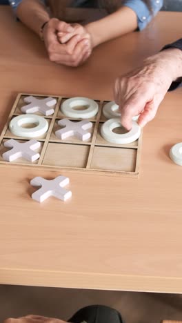 senior friends playing tic tac toe at table in nursing home
