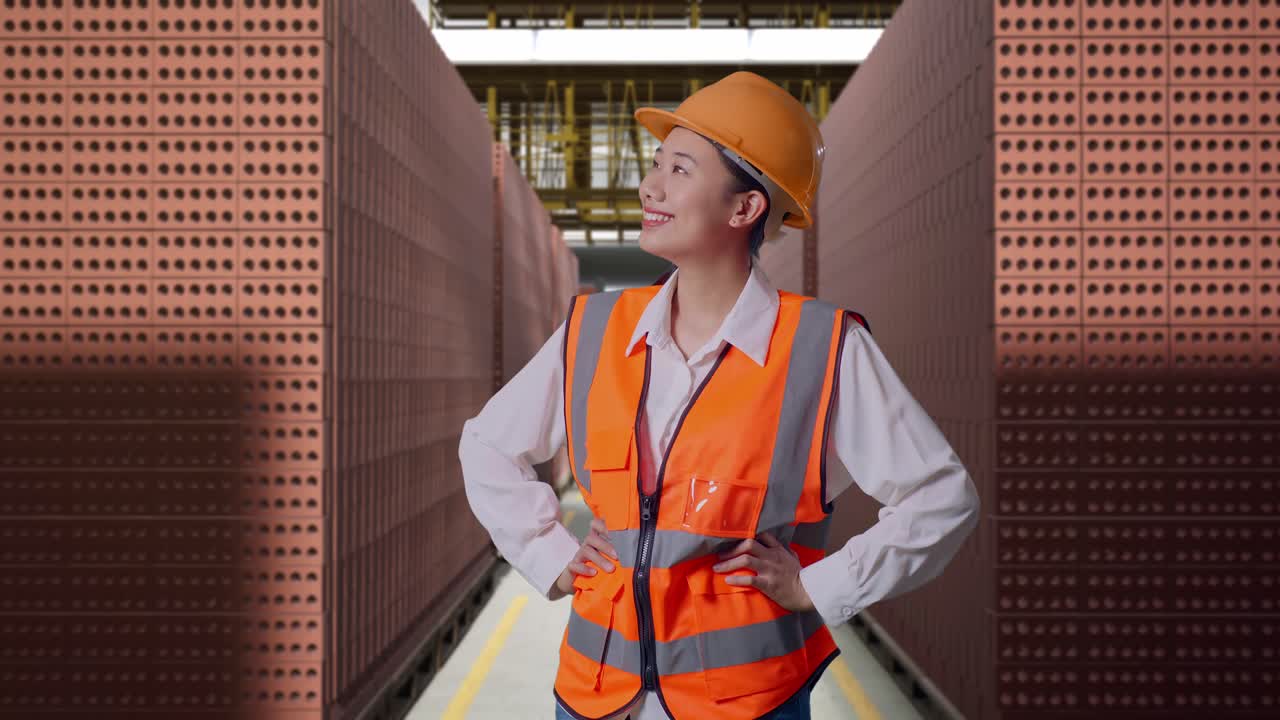 Asian Female Engineer Wearing Safety Helmet Looking Around While Standing With Arms Akimbo With Red Brick Packed in Stacks Are Stored
