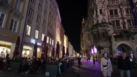 a wide-angle night view of munich, capturing people shopping and sightseeing beneath an illuminated building.