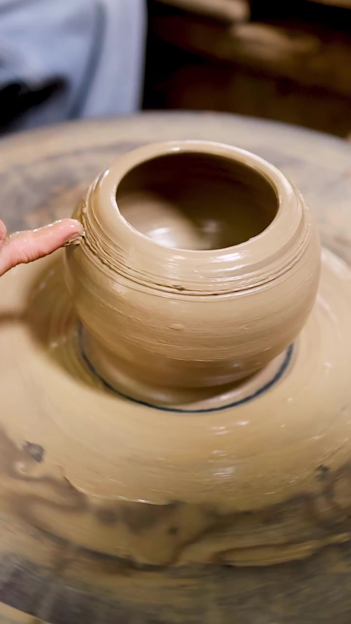 Primo piano di mani che intagliano linee decorative su un vaso di argilla rotante in uno studio