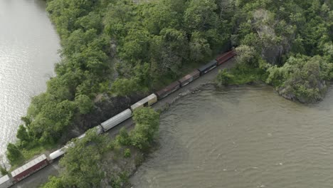 drone shot of a long cargo train going into a tunnel, flying down and panning to the left