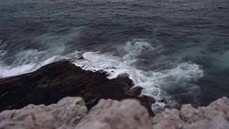 atlantic ocean waves washing up against rock along european coast - static evening clip looking down at ocean after sunset with light colored cliff in foreground close to camera