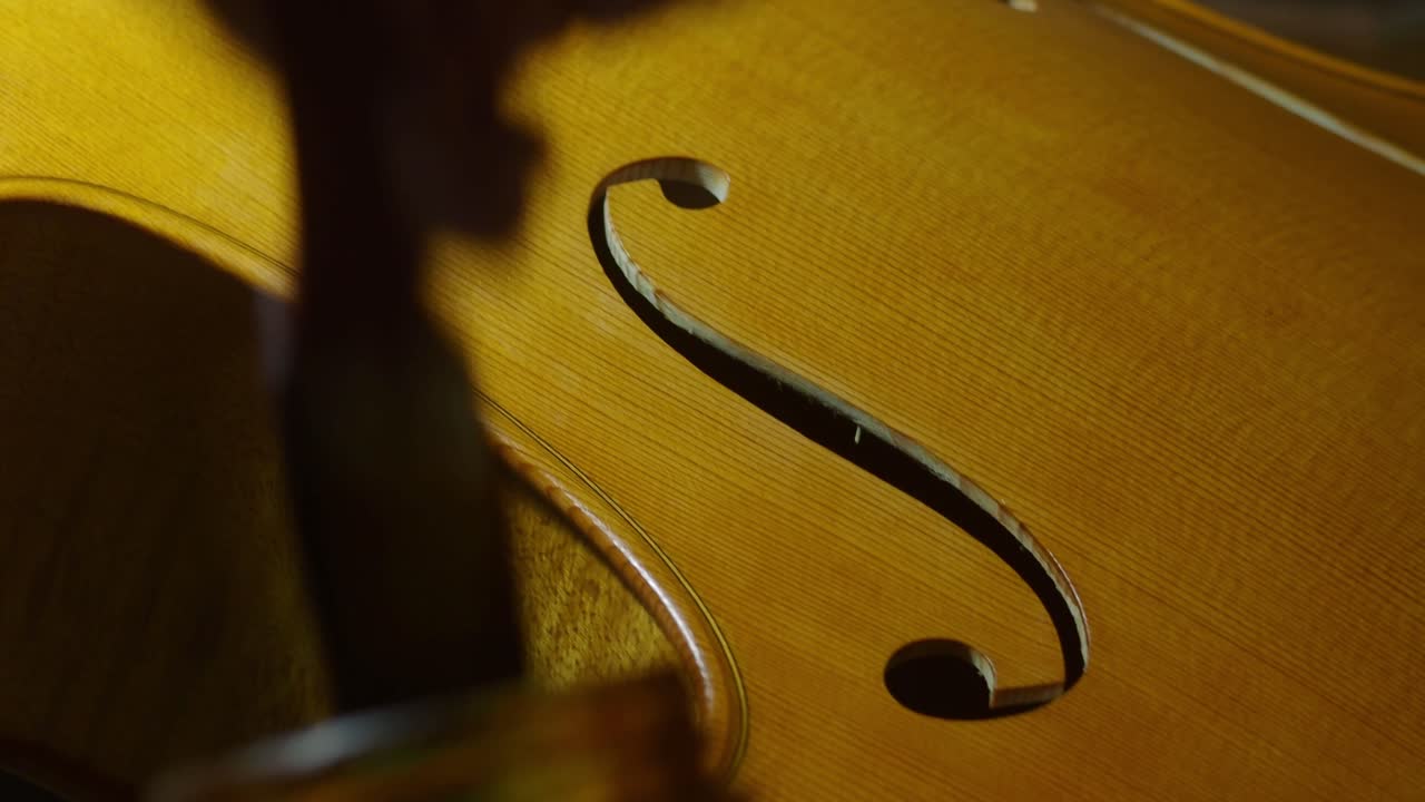 Close up of a luthier's meticulous varnish work on a cello's sound F hole and top plate, showcasing the precision and artistry involved in crafting musical instruments
