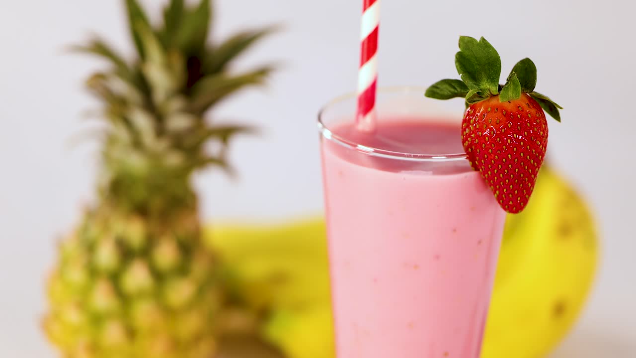 Pink smoothie in clear glass with strawberry, pineapple, banana, bright lighting, static camera