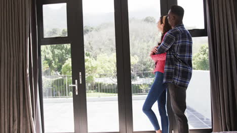 una pareja feliz y diversa mirando por la ventana, sonriendo y abrazándose, cámara lenta, espacio de copia