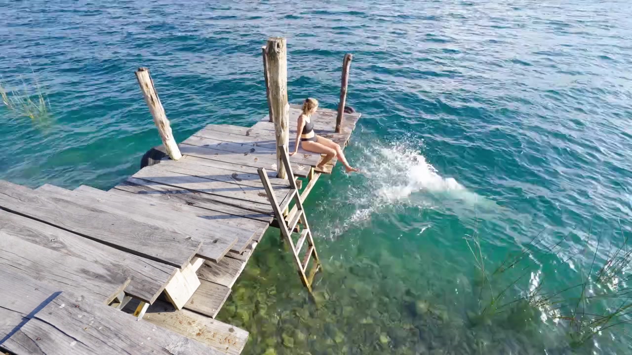 Folk hopper i klart vand fra en rustik træmole ved Atitlán-søen på en solrig dag i Guatemala.