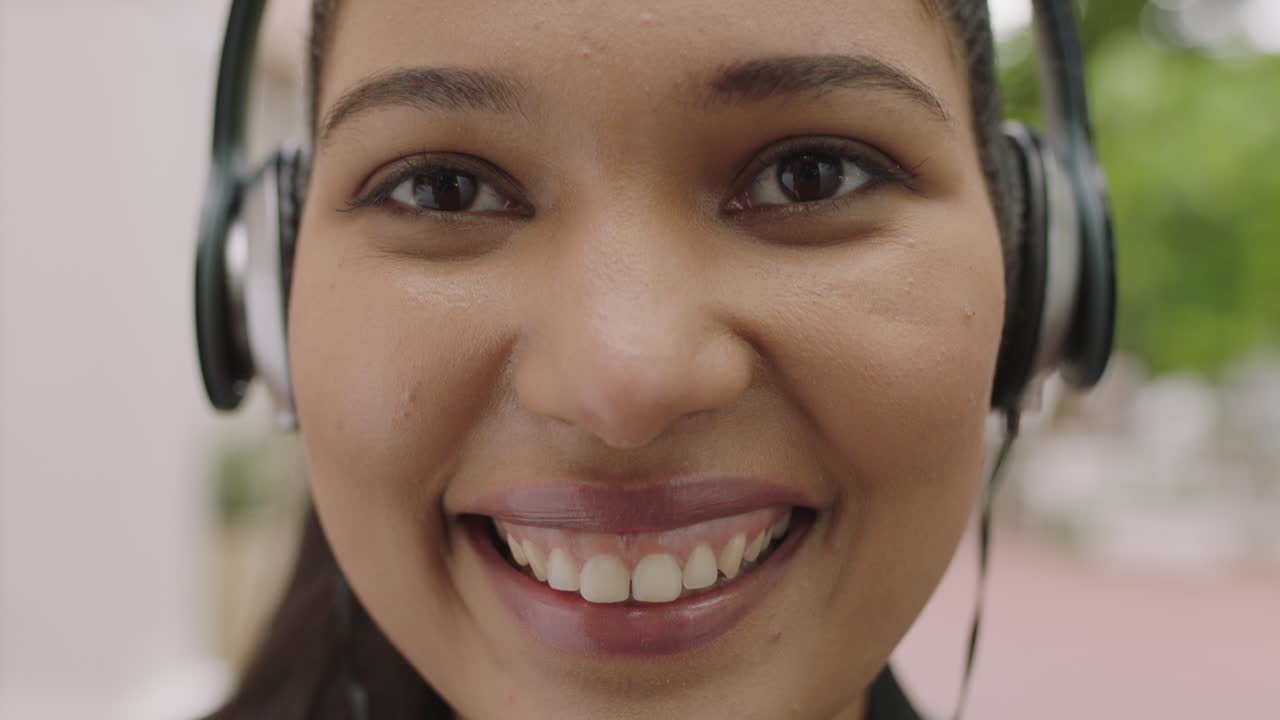 retrato en primer plano de una hermosa mujer de raza mixta sonriendo feliz mirando a la cámara con auriculares escuchando música disfrutando de un estilo de vida urbano relajado