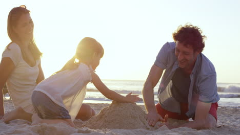 happy family playing on the beach building sand castle at sunset