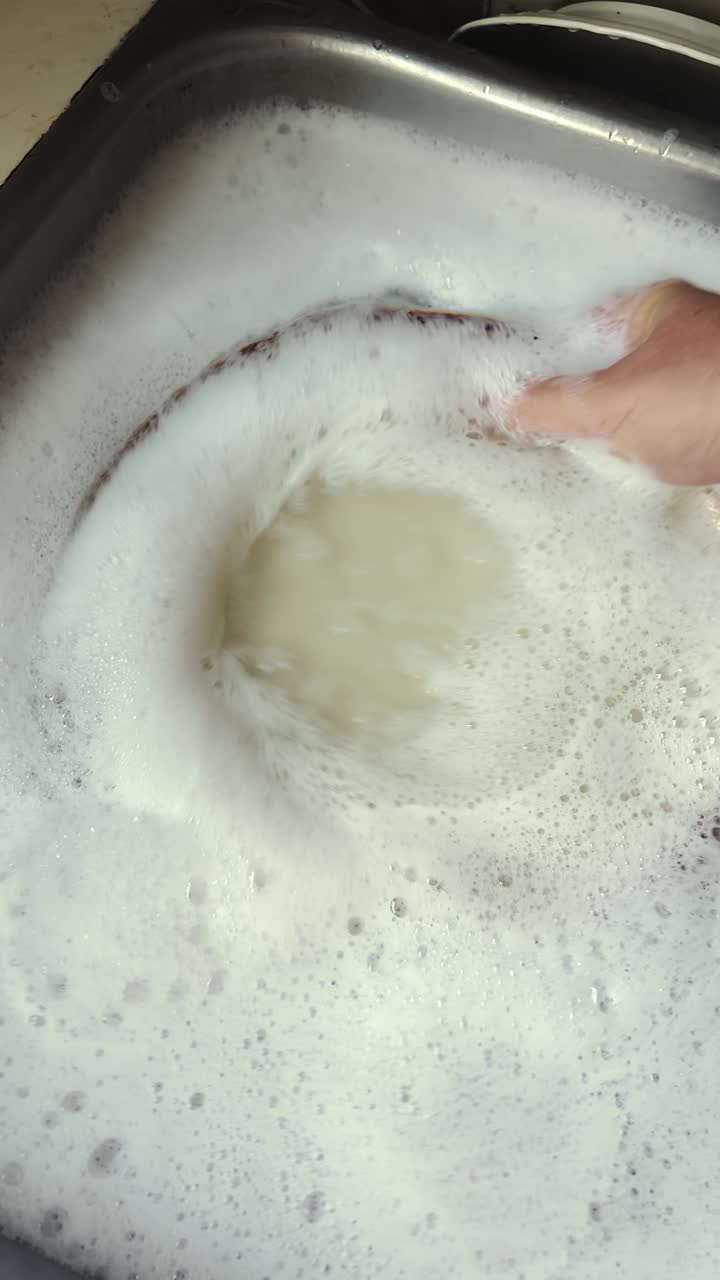 Hygienic person washing dishes in foamy soapy water Vertical shot