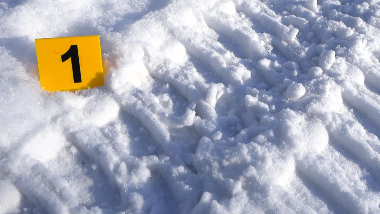 Un segnalatore numerato di prova o tendina si trova accanto a profonde tracce di pneumatici mentre la luce solare intensa rivela la texture scintillante della neve.