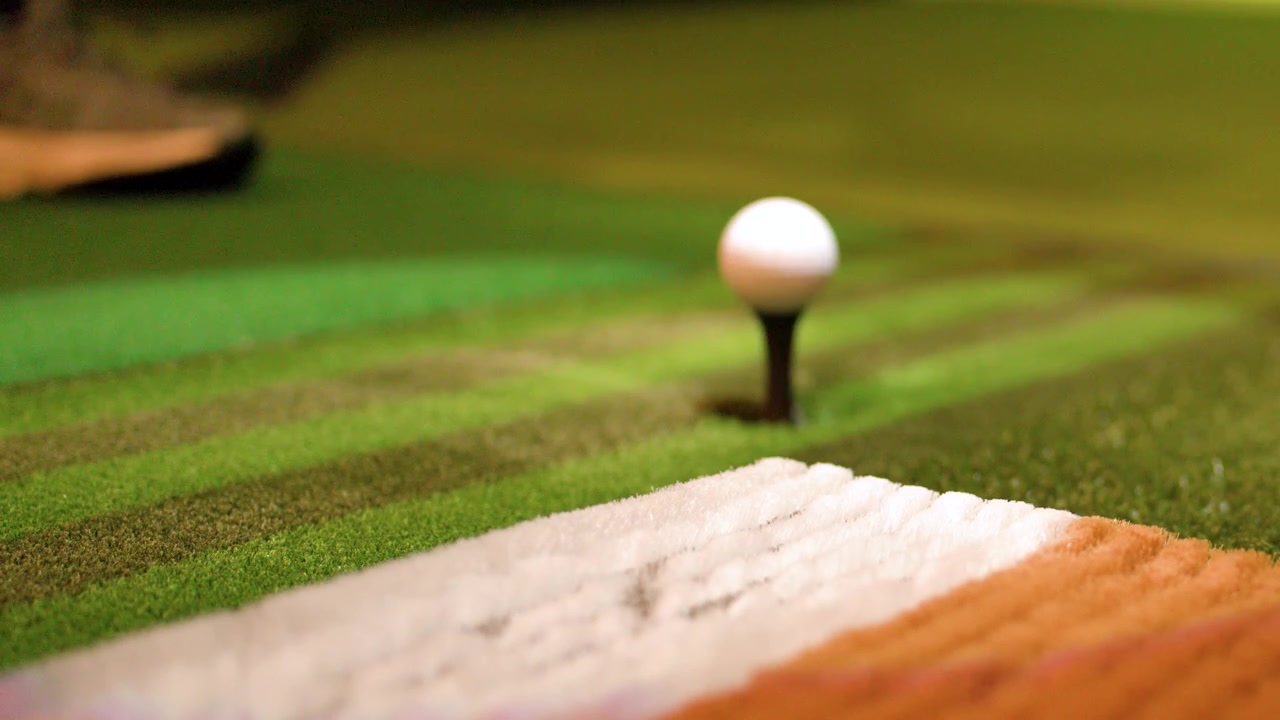 Et golfjern slår en ball på en kunstgressmatte inne i et simulatoranlegg