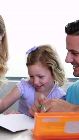 padres sonrientes y hija dibujando en la mesa