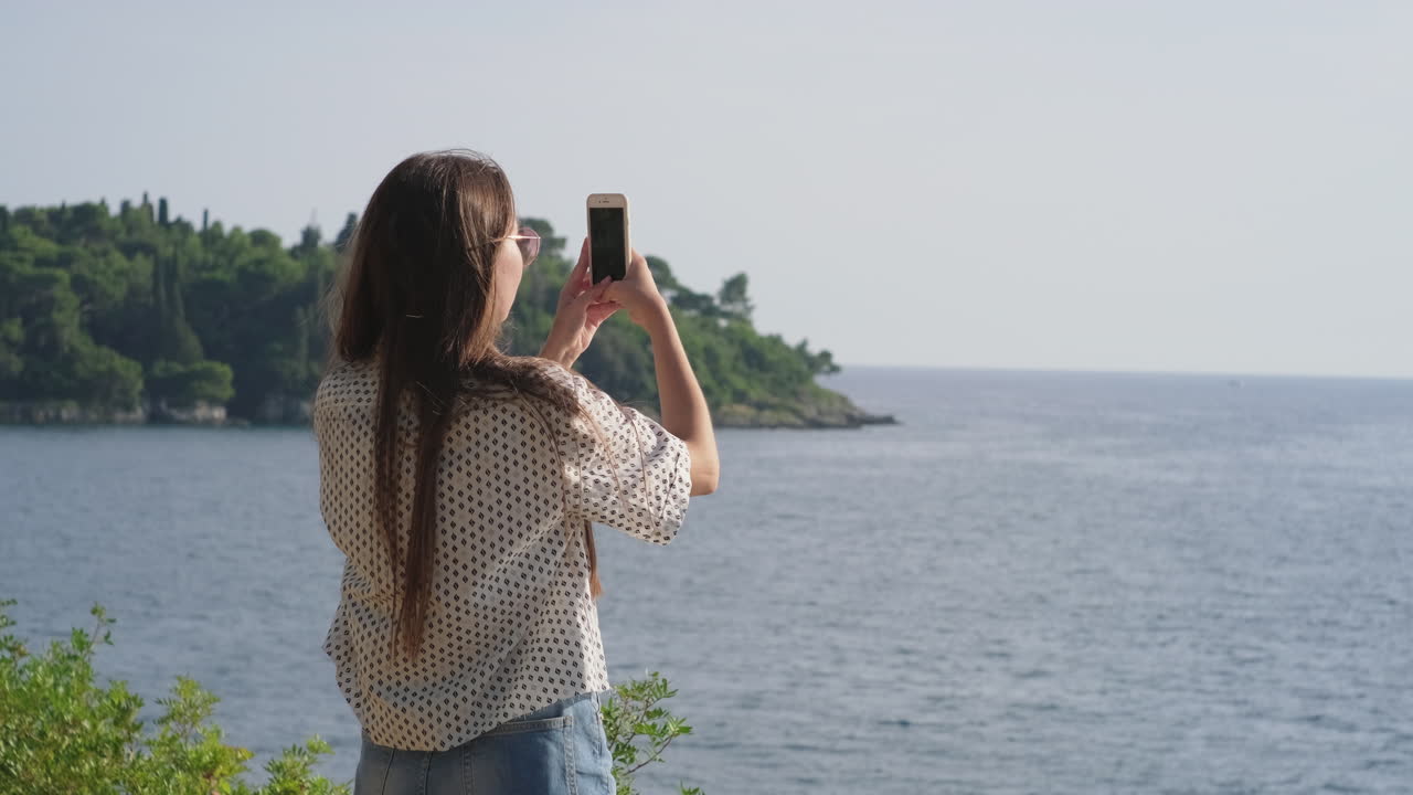 mujer tomando una foto de la vista panorámica de la costa
