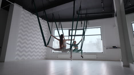 entrenador y mujer joven practicando gimnasia aero con suspensiones en el gimnasio. grupo de dos jóvenes mujeres hermosas yogi haciendo práctica de yoga aéreo en hamacas verdes en el club de fitness