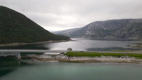 toma aérea rastreando un auto conduciendo a través de un puente sobre un lago con montañas