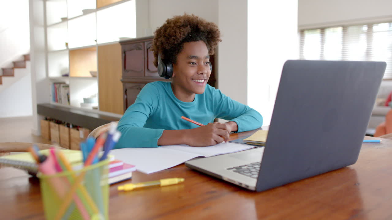 niño afroamericano con auriculares, usando portátil para clases en línea, cámara lenta