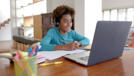 african american boy wearing headphones, using laptop for online class, slow motion