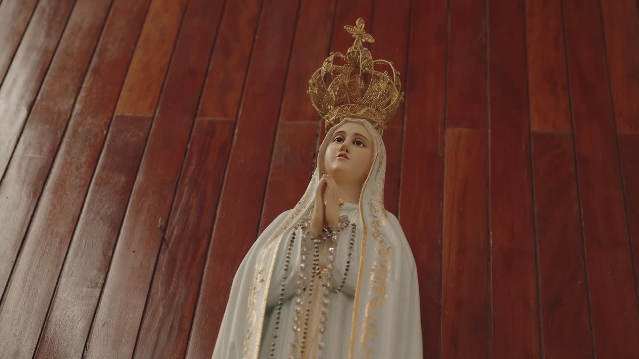 Close up crowned statue of Our Lady holding rosary in prayer against polished wooden wall background