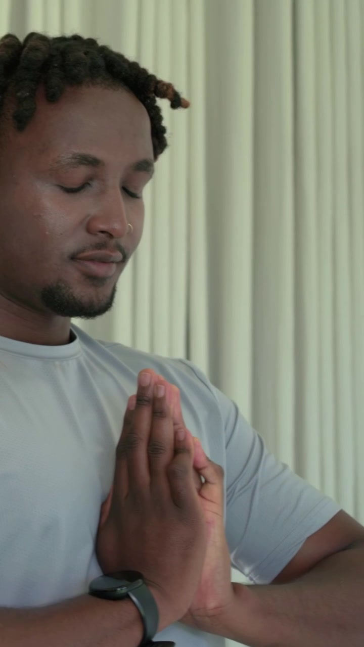 Vertical video: Joining palms adult man centering and closing eyes by window with watch and nose r