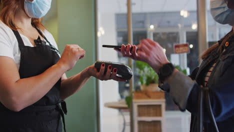 Female-customer-paying-to-Female-hairdresser-using-smartphone-at-hair-salon