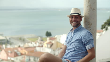 medium shot of happy man sitting on observation tower, looking at the city and then, to the camera