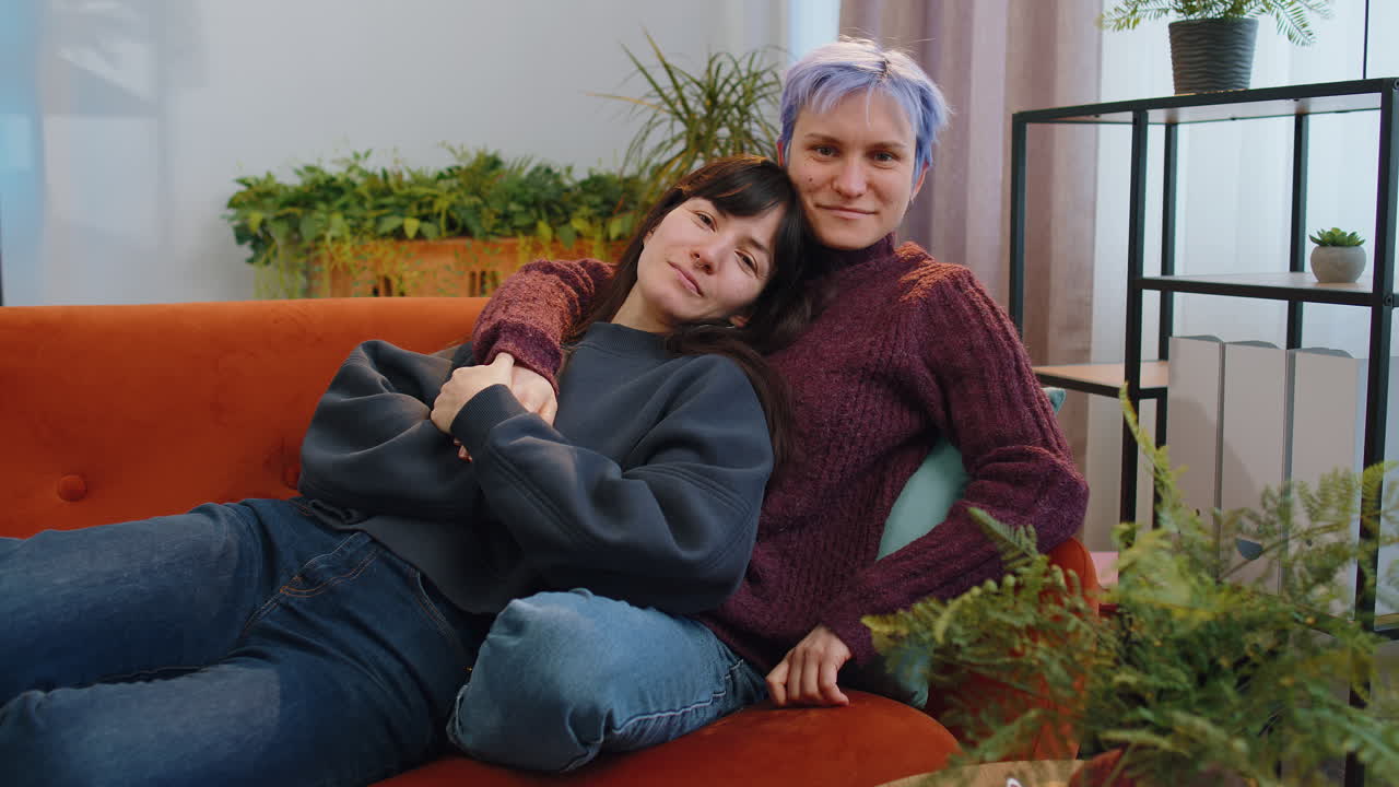Loving same sex female lesbian women family couple hugging relaxing together lie on sofa at home