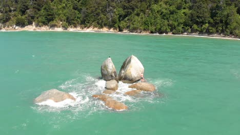 aerial clip of a portion of the ocean in the abel tasman national park, with a rock in the foreground with the curious form of a split apple