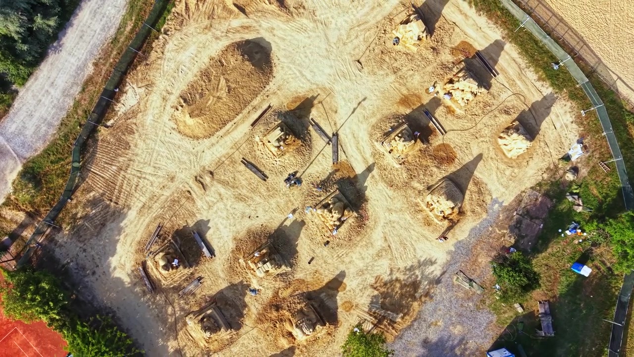 Eine Baustelle zeigt Arbeiter, die tagsüber in einer ländlichen Gegend den Boden vorbereiten und Strukturen errichten.