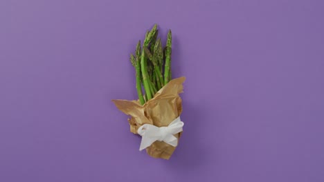 video of fresh asparagus wrapped with white ribbon and copy space over lilac background