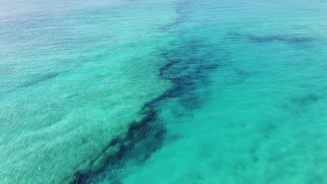 Drone-flight-over-crystal-clear-turquoise-water-with-a-view-to-the-reef-underwater,-in-Cape-Verde