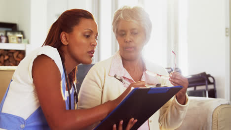 Doctor-explaining-medication-on-clipboard-to-senior-woman-in-living-room-4k