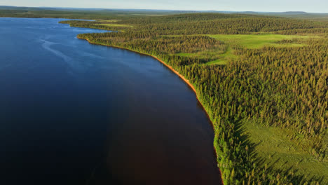 Drone-Inclinándose-Desde-Una-Playa-De-Arena-Roja-En-El-Lago-Pallasjarvi,-Puesta-De-Sol-En-Laponia