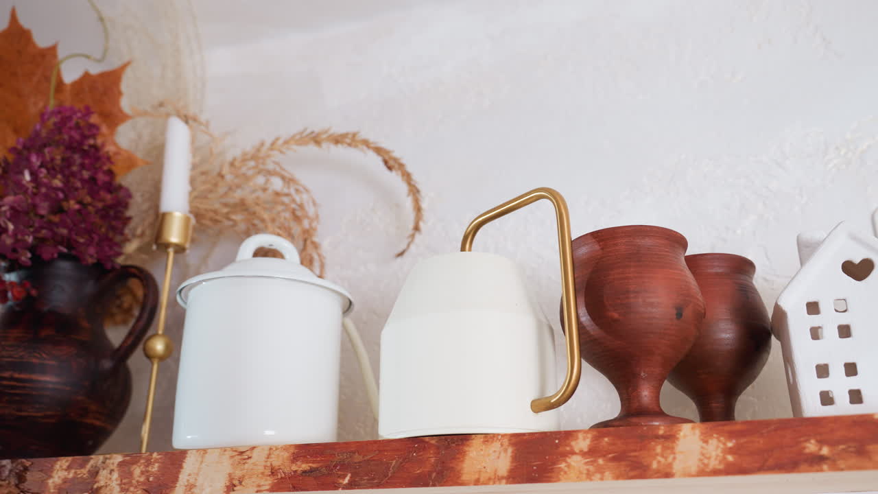 Neatly arranged different flower vessels and rustic decor items including ceramic jugs, wooden goblets, dried floral bouquet, candle holder, and mini decorative house on wooden shelf
