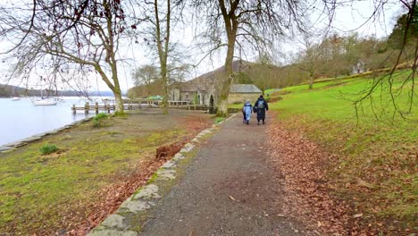 Turistas-Caminando-Por-Un-Sendero-Al-Pie-De-La-Caída,-Cumbria,-Lago-Windermere-Con-Su-Cautivador-Embarcadero-De-Madera