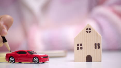 close-up of a hand holding a pencil and writing something on a yellow paper, behind a red toy car that signifies car loan financing