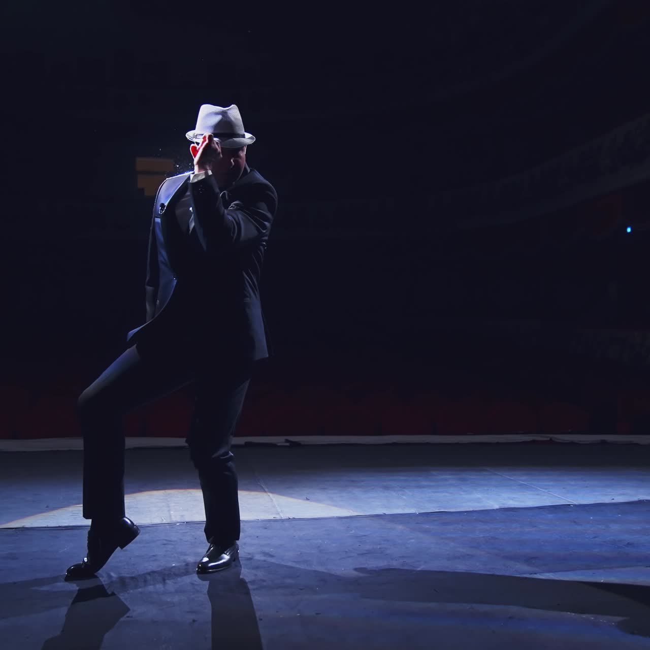 Actor in hat on stage. Active man in costume dancing on stage on dark background at spotlight. Theatrical man performing show.
