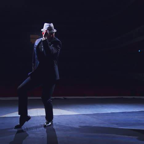 actor in hat on stage. active man in costume dancing on stage on dark background at spotlight. theatrical man performing show.