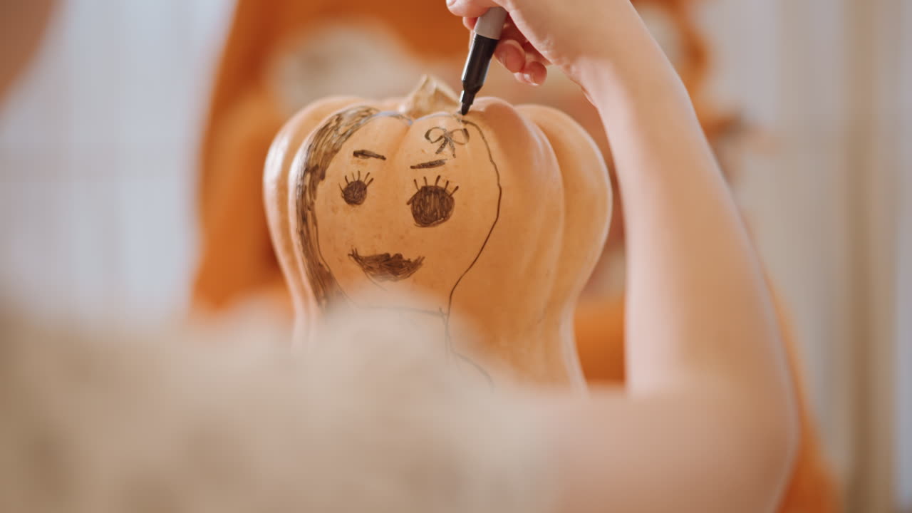 Primo piano di mani che disegnano una faccia su una zucca con un pennarello, in una calda ambientazione casalinga autunnale. Luce naturale soffusa e tessuti texturizzati. Schizzo e inchiostrazione passo dopo passo di un sorriso giocoso su una zucca a coste, con un gesto delicato della mano.