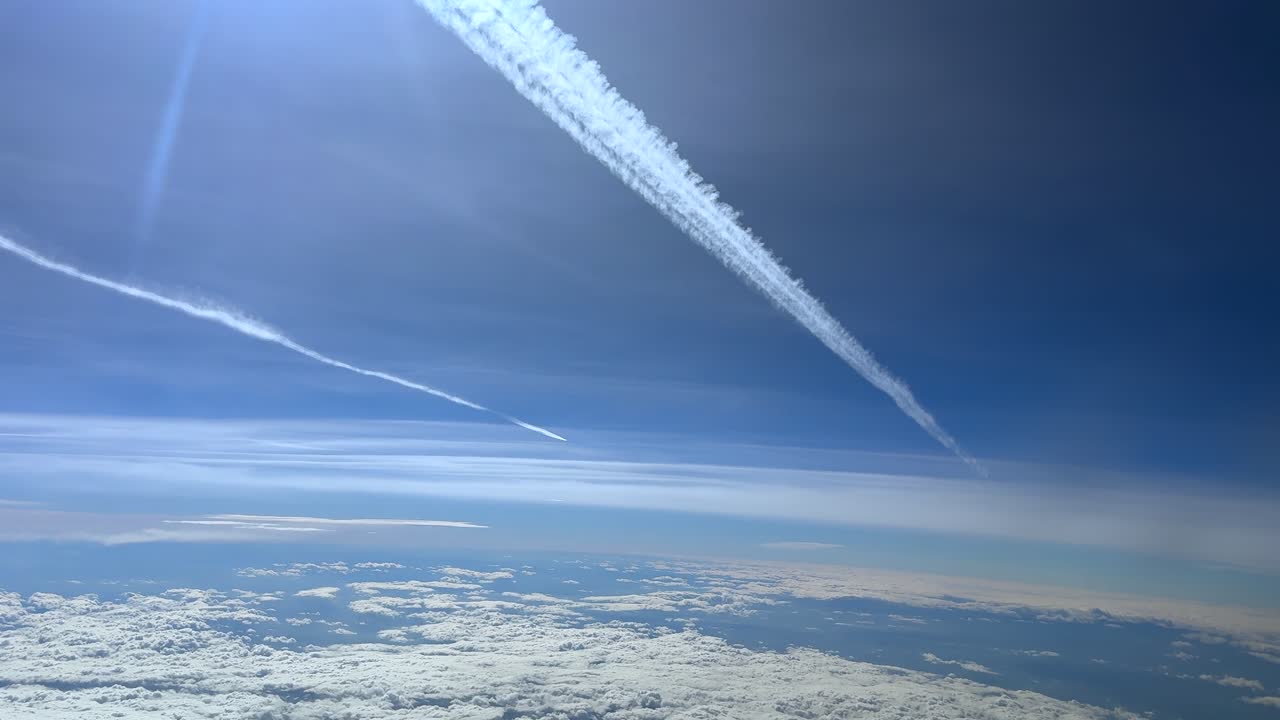 コックピットから撮影された臨場感あふれるジェット機の横断。青い空に飛行機雲を残し、日光が降り注ぐ情景。