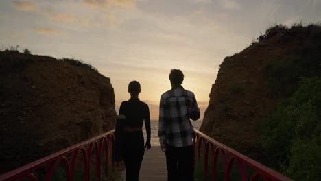 couple walking on a beach bridge at sunrise