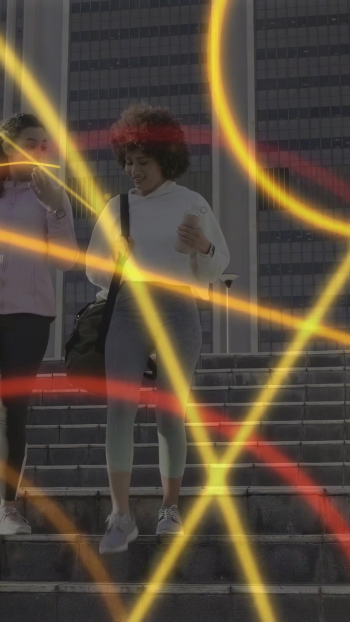 Video verticale: Due donne che scendono le scale, camminando verso la palestra mentre anelli al neon incorniciano i borsoni.