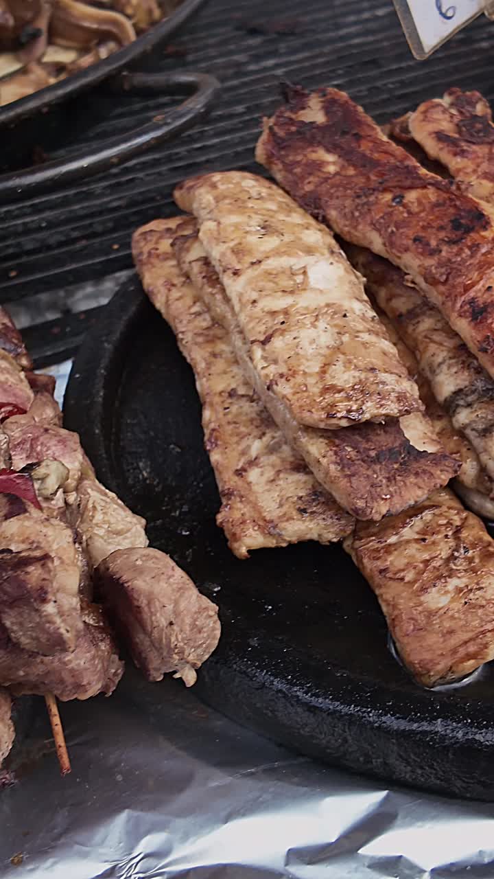 Panoramica verticale ravvicinata su spiedini shish kebab grigliati e maiale a un festival all'aperto bulgaro. Ideale per temi di cucina culturale, gastronomia tradizionale e catering per eventi.