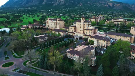 broadmoor buildings nestled in green canopy with reflective water and bright skies, aerial orbit